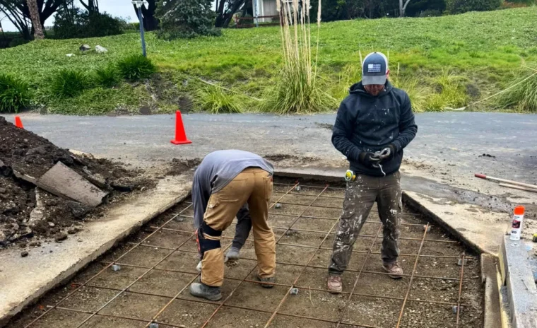 Two construction workers preparing a concrete pad with rebar and gravel on a worksite.