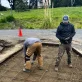Two construction workers preparing a concrete pad with rebar and gravel on a worksite.